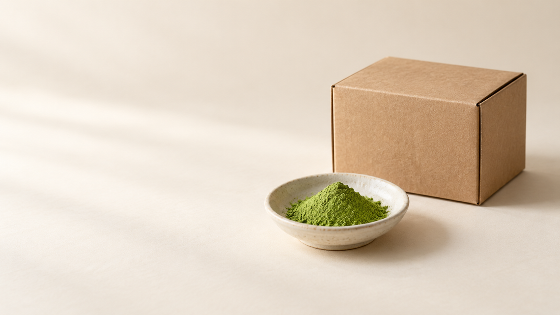 Matcha powder in a ceramic dish beside a plain kraft shipping box.