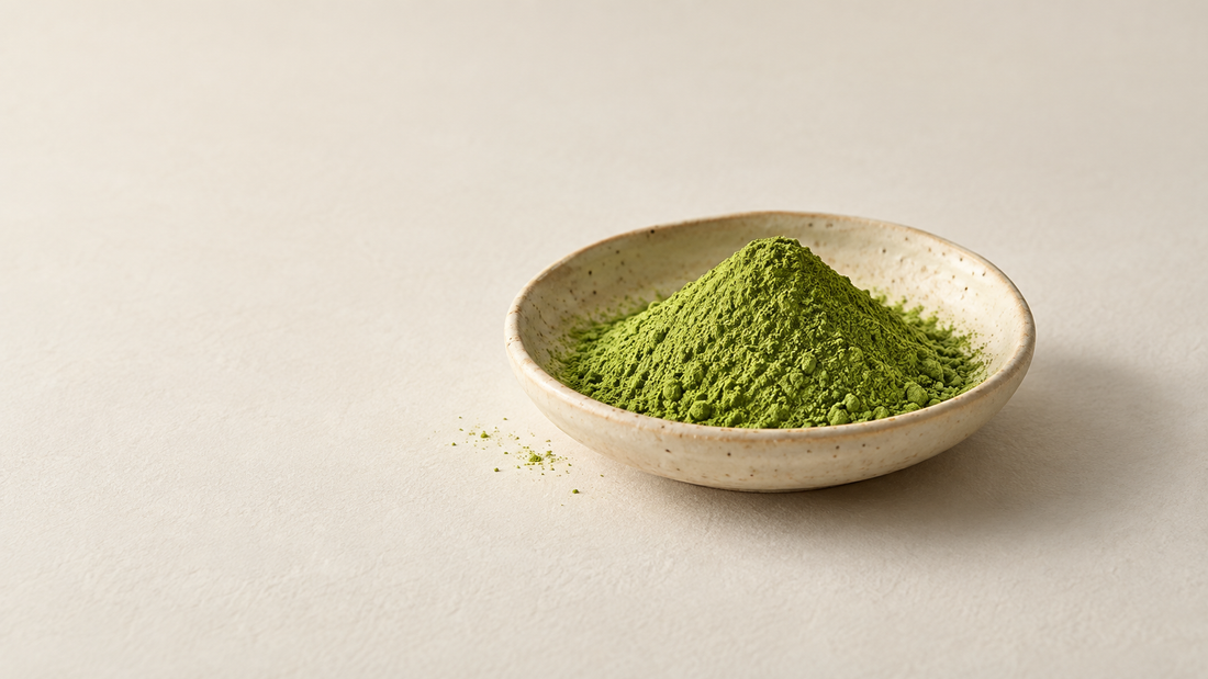 Fine green matcha powder in a shallow ceramic dish on an ivory background.