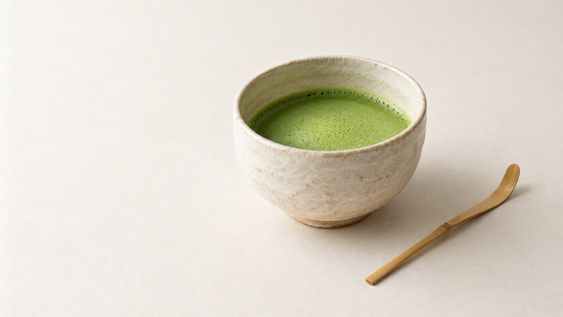 Freshly whisked matcha in an ivory ceramic bowl beside a bamboo tea scoop.